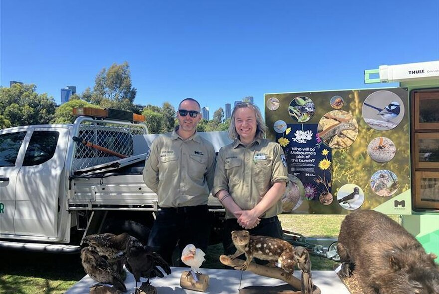 Two park rangers in front of a display table with their ute behind and more displays.