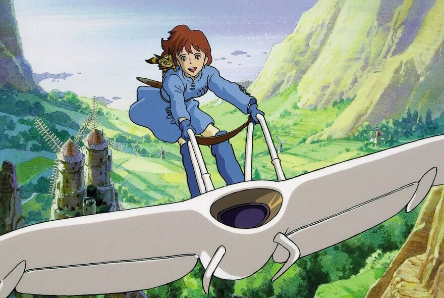 A still from a Studio Ghibli animated film of a child standing on top of a glider that is moving through the air high above green fields and valleys below it.