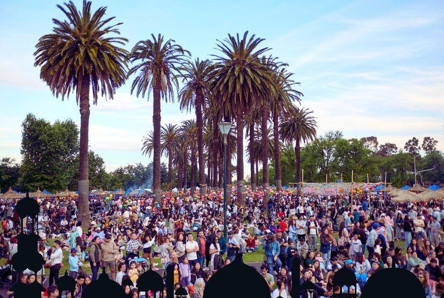 A large crowd in public gardens with palm trees and blue skies behind them.