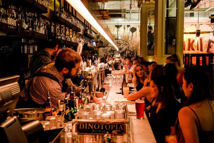 Looking down a bar with patrons on one side and bar staff on the other side, with many glasses and beer taps.