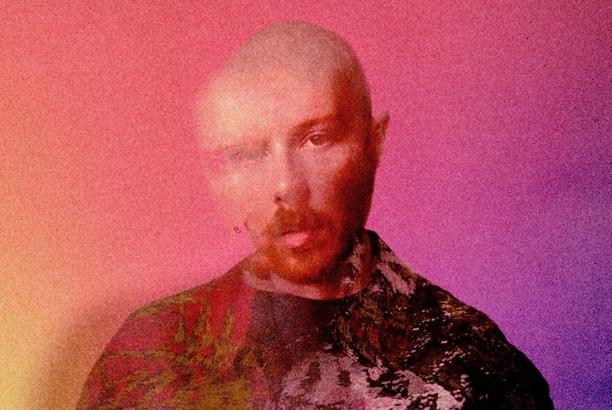 Slightly distorted and blurred image of musician Matthew Barnes, a middle-aged man with a shaved head, a mustache, posed in front of a pinkish-orange background.