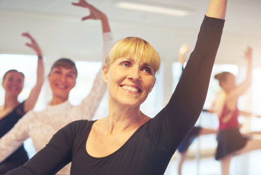 Smiling women in a ballet studio practicing ballet exercises at the barre.