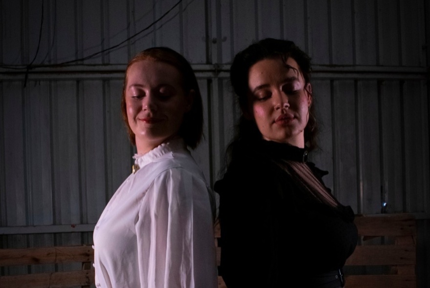 Actors dressed in 19th-century dresses, standing back to back.