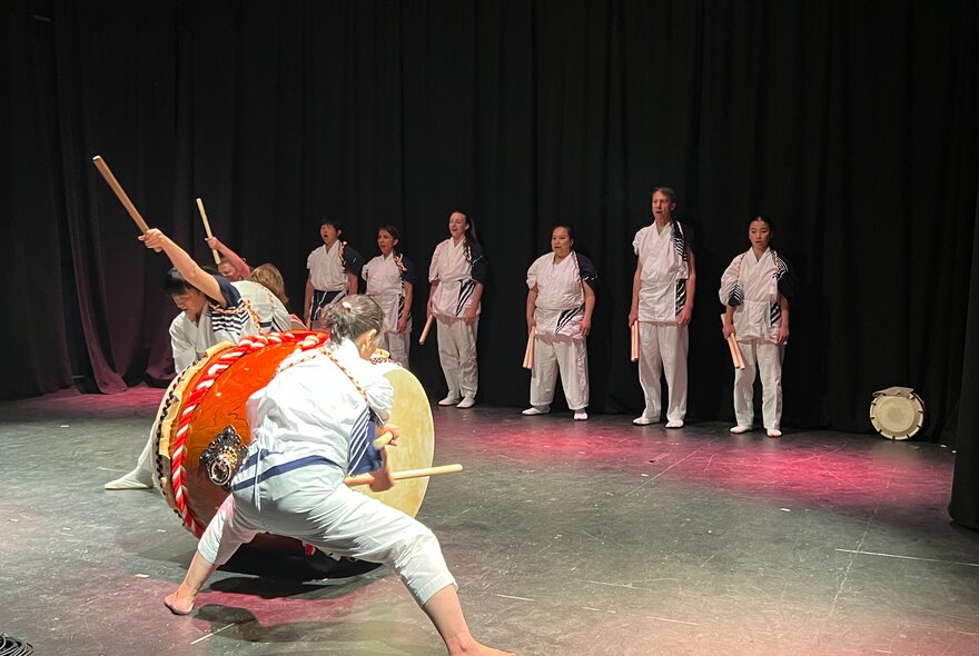 Traditional Korean dancers on stage with a line of dancers watching from the side.