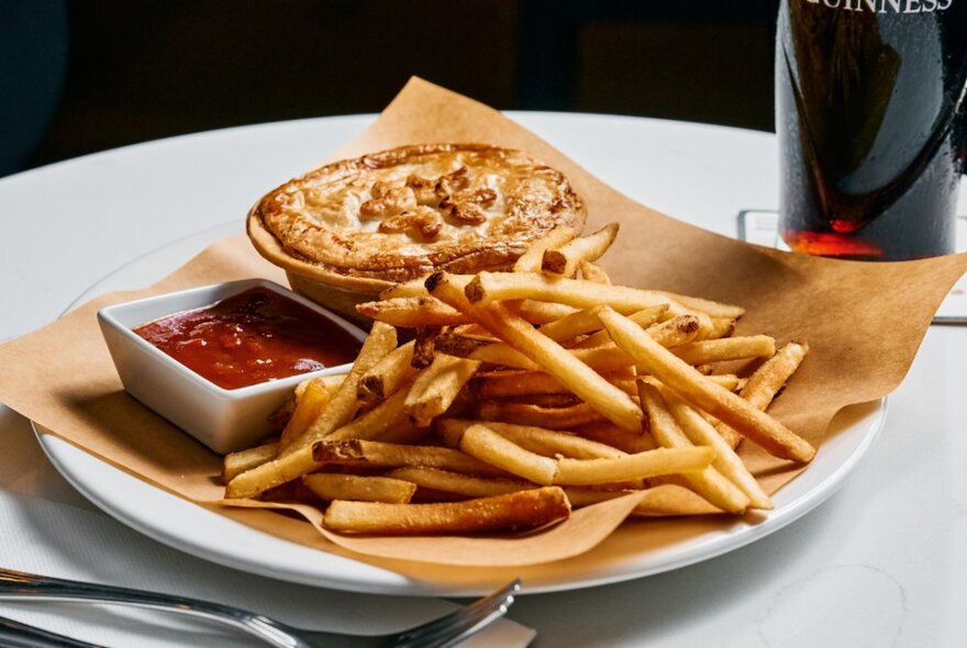 A pie with chips and sauce on a serviette on a plate on a table.