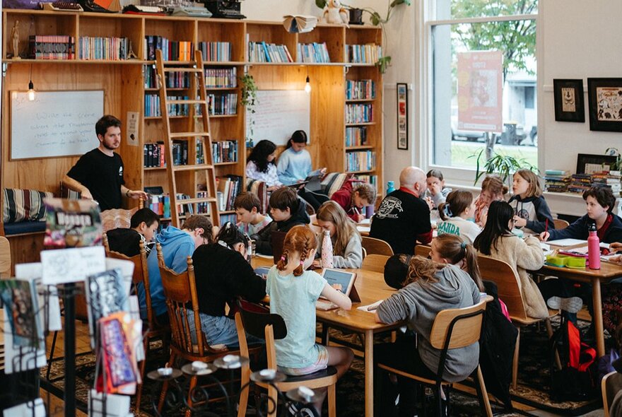 Kids in a classroom setting at desks with a teacher at the front. 