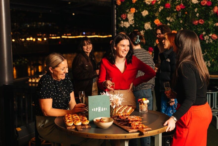 A group of women standing around a tall round table set with plates of canapes.