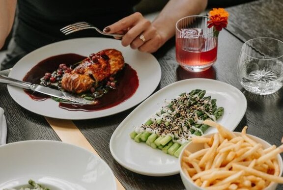 A person's hand holding a fork over a plate of food at a restaurant dining table.