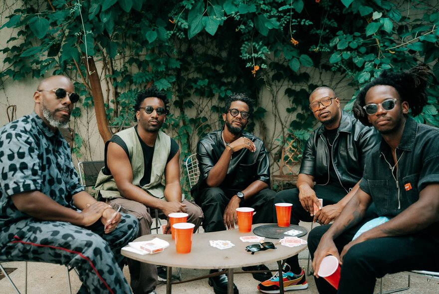 A collection of jazz musicians sitting around a coffee table with orange cups on it.