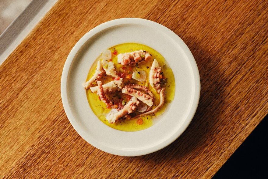 Cooked octopus tentacles served on a white plate, on a wooden table top.