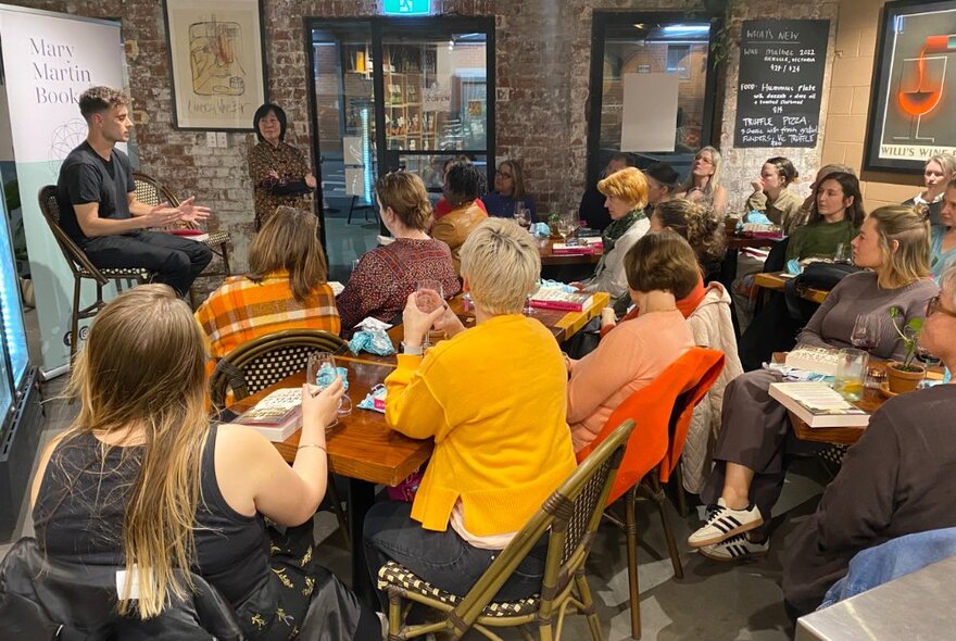 A small gathering of people seated listening to an author discussing their book. 