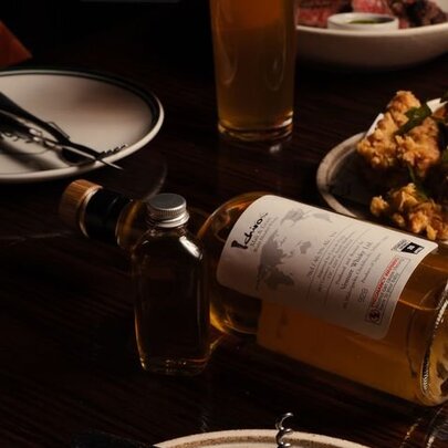 A dark and moody tabletop with a whisky bottle on its side between plates of food.