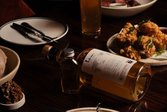 A dark and moody tabletop with a whisky bottle on its side between plates of food.