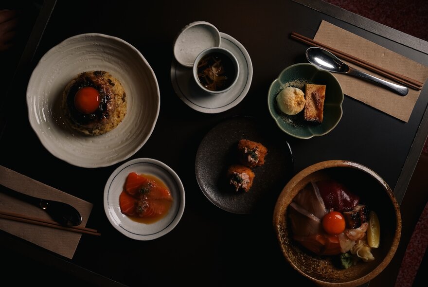 A restaurant table with plates of food, small bowls of condiments and side dishes, and cutlery resting on napkins.