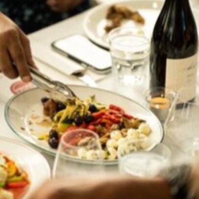 Hand serving from a dish of Italian food with wine and glasses on a restaurant table.