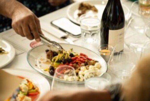 Hand serving from a dish of Italian food with wine and glasses on a restaurant table.