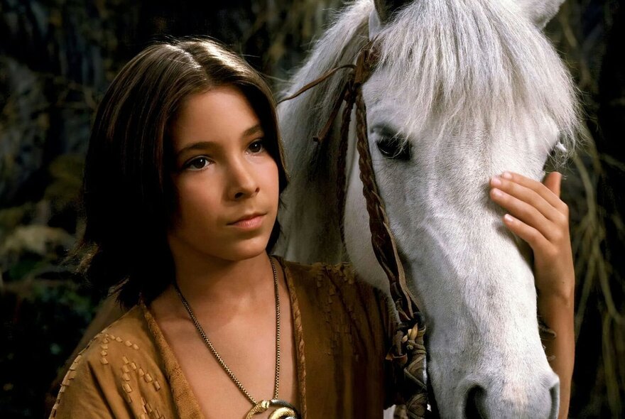 A child stroking the forehead of a white horse.
