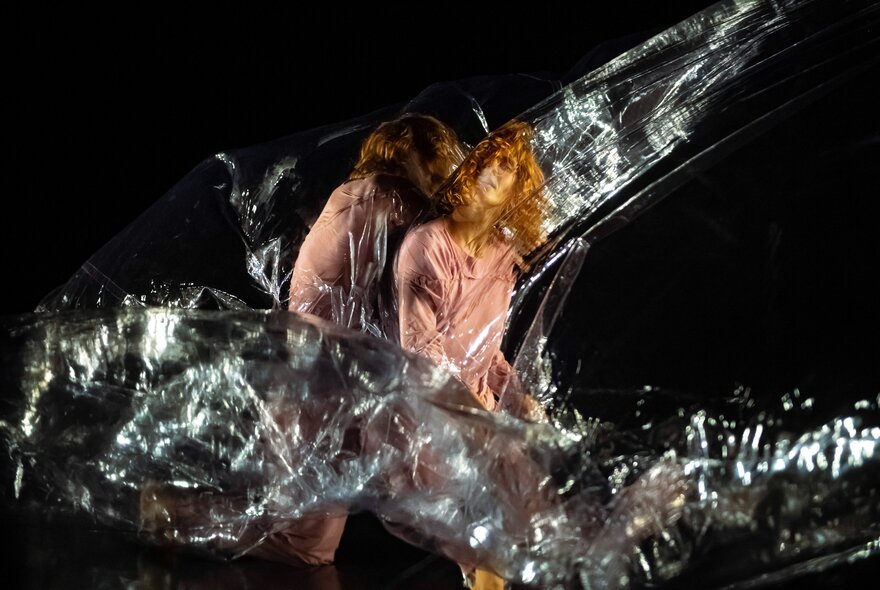 A scene from the contemporary dance work Red by Australian company Dancenorth, with two dancers standing wrapped in clear plastic  on a dark stage.