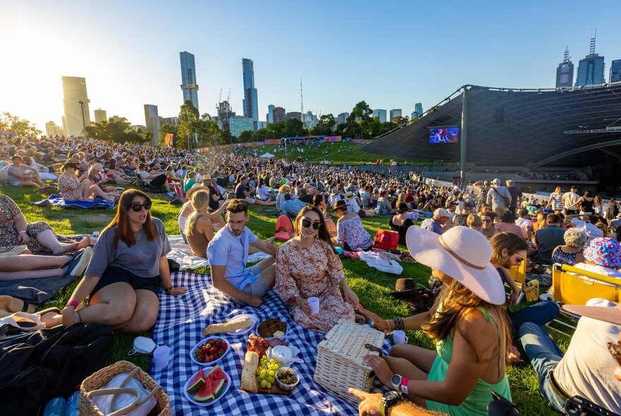 A group of friends having a picnic amongst a crowd of people sitting on the grass at an outdoor music venue in Melbourne.