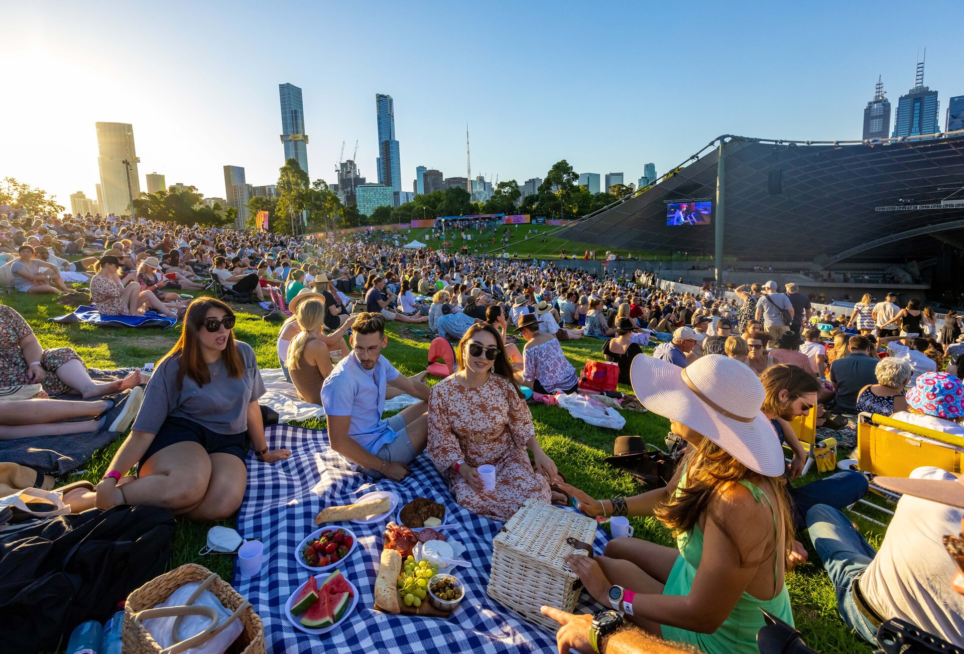 A group of friends having a picnic amongst a crowd of people sitting on the grass at an outdoor music venue in Melbourne.