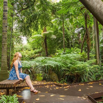 Woman in blue dress sitting in a garden, with face upturned.