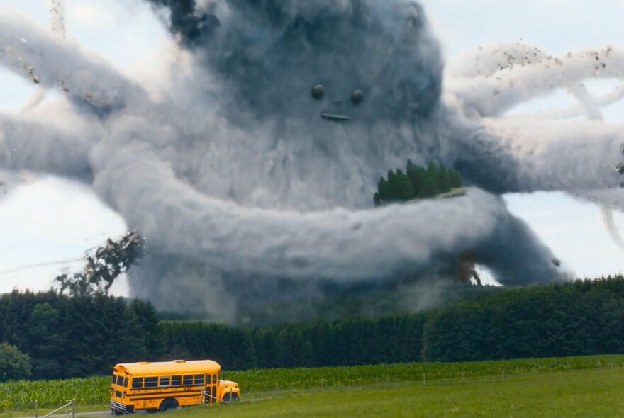 A yellow schoolbus parked on grass with a fierce spider-like giant grey cloud on the horizon.