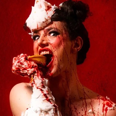 Saucy woman biting into a pie with cream and red sauce like blood dripping over her face and shoulders.