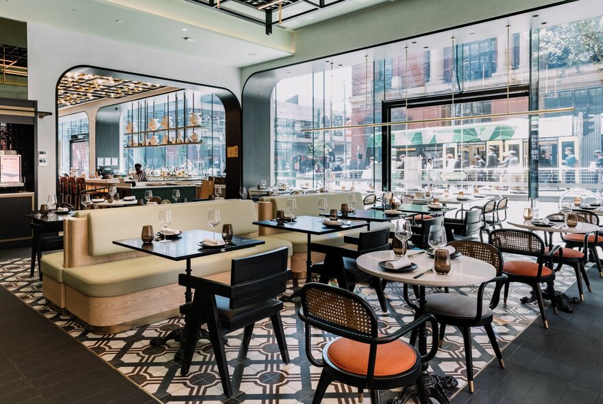The light-filled interior of Miss Mi restaurant, with dining tables and chairs, some banquette seats, and expansive floor to ceiling windows with views onto the street.