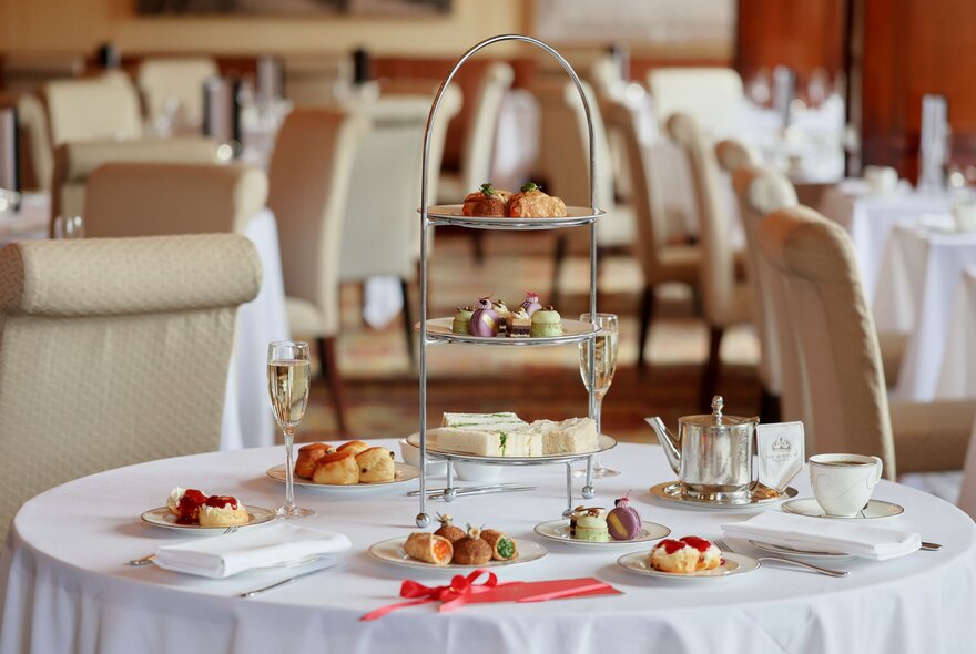A formal round table set for afternoon tea with empty tables and chairs blurred in the background. 