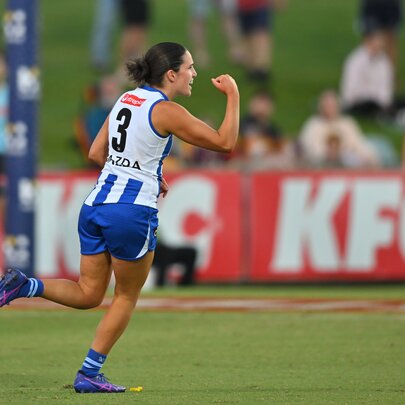 A North Melbourne AFLW player celebrating and cheering herself on the field with a raised and clenched fist.