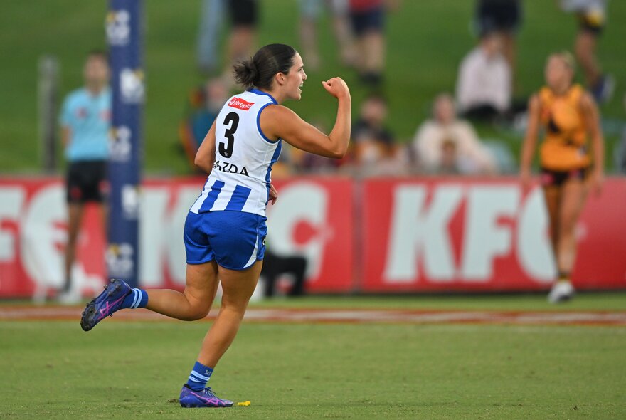 A North Melbourne AFLW player celebrating and cheering herself on the field with a raised and clenched fist.