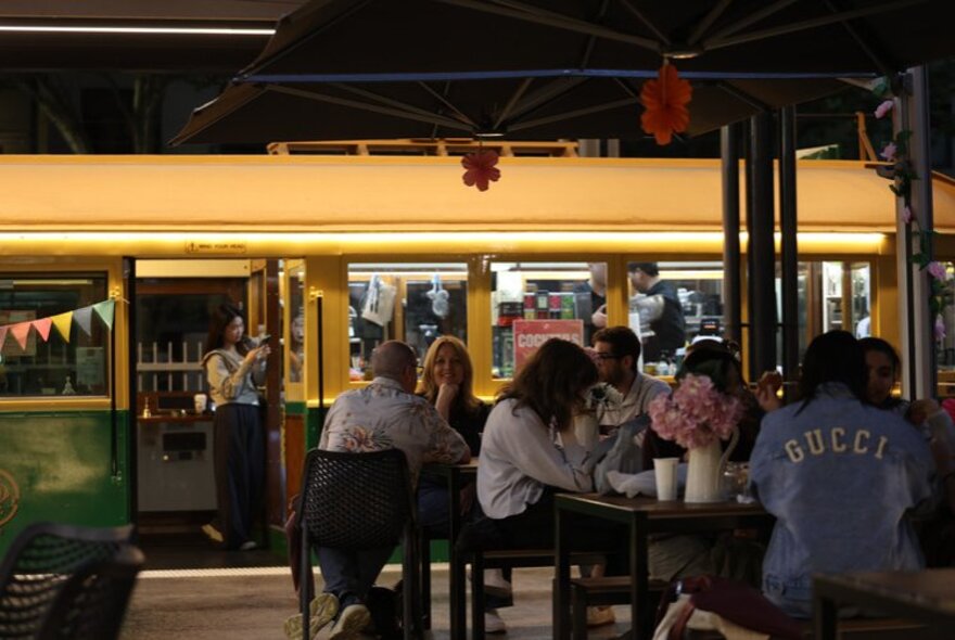 People seated at cafe tables next to a vintage Melbourne tram.