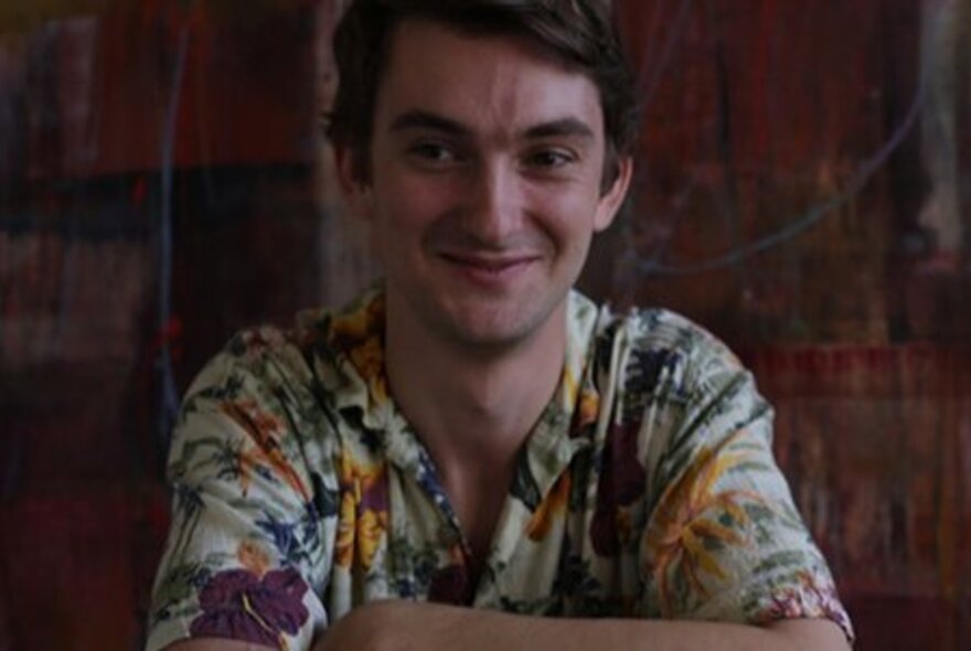 Man wearing patterned shirt, smiling with his arms folded.