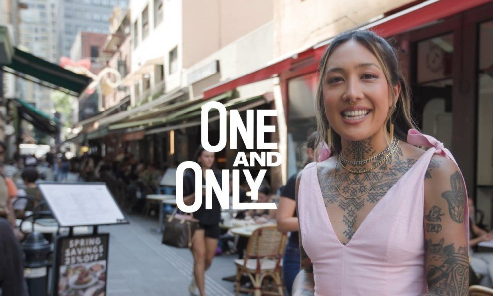 A tattooed woman standing in a Melbourne laneway with the text "One and Only" in the centre of the photo. 