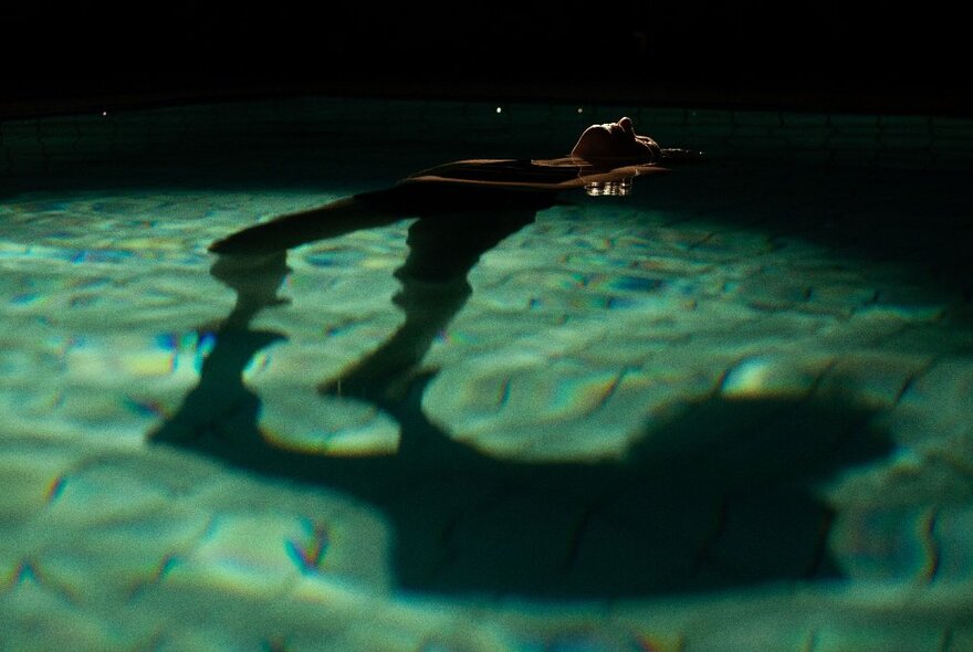 A person floating in a darkened pool, listening to underwater music.