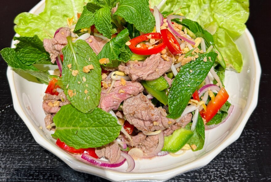 Looking down plate containing sliced beef, chillies and mint leaves in a salad.