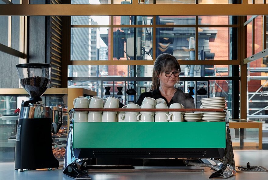 Barista standing behind a coffee machine, equipment and crockery in a hotel setting.