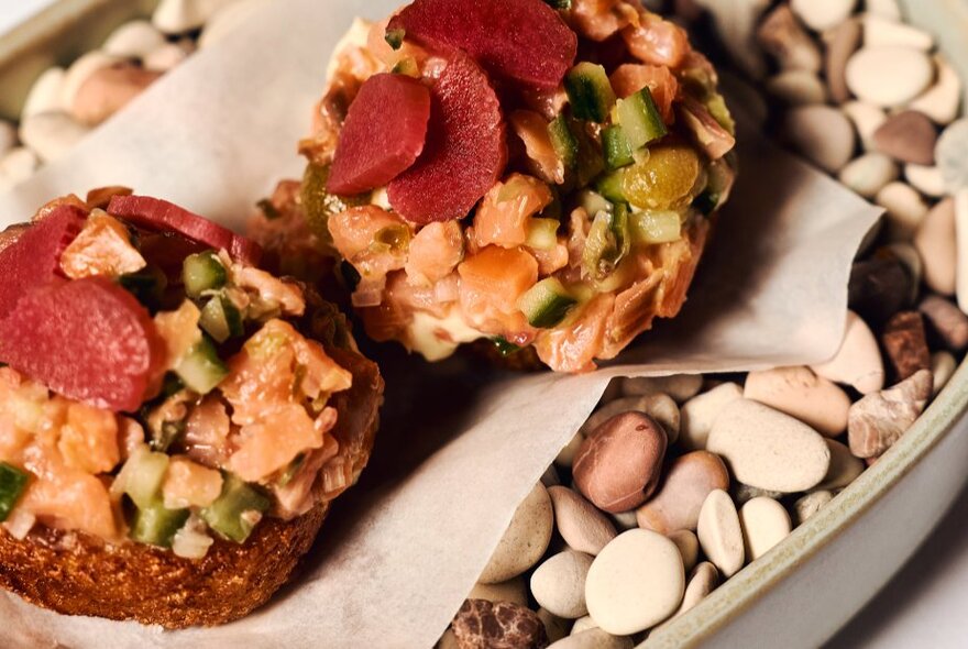 Open-topped sandwiches on a tray of pebbles.