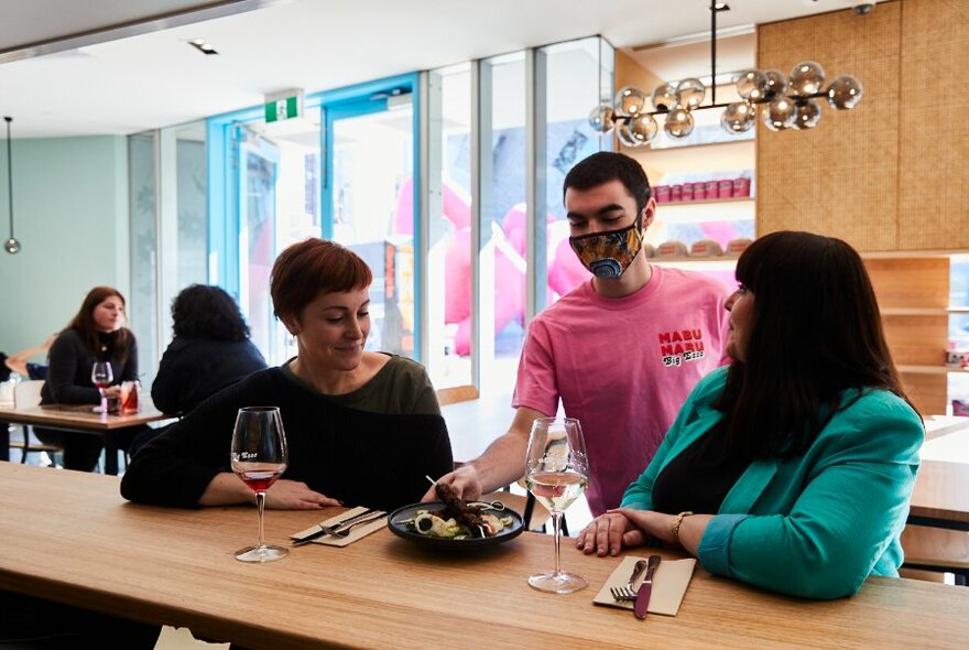 Two diners in a bright restaurant being served food. 