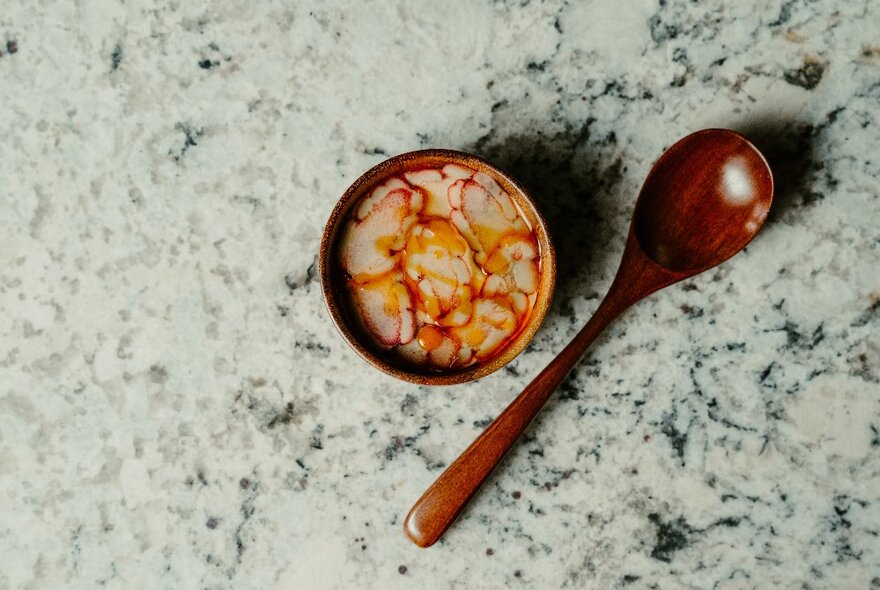 A small bowl of food with a wooden spoon next to it, resting on a marble dining table.