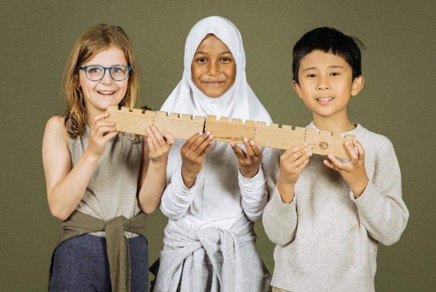 Three kids looking happy holding a long wooden bar.