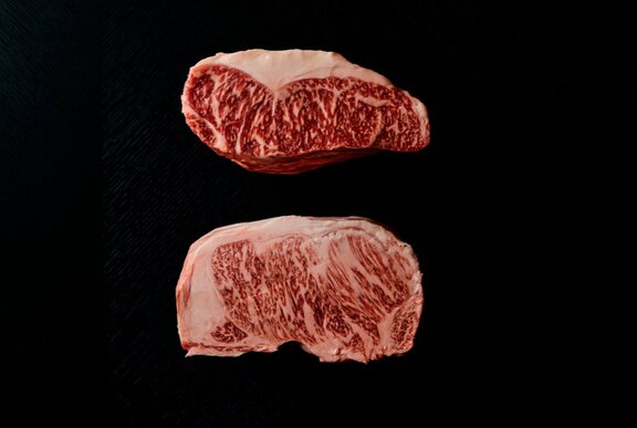 Slabs of raw marbled Wagyhu beef on a black background.