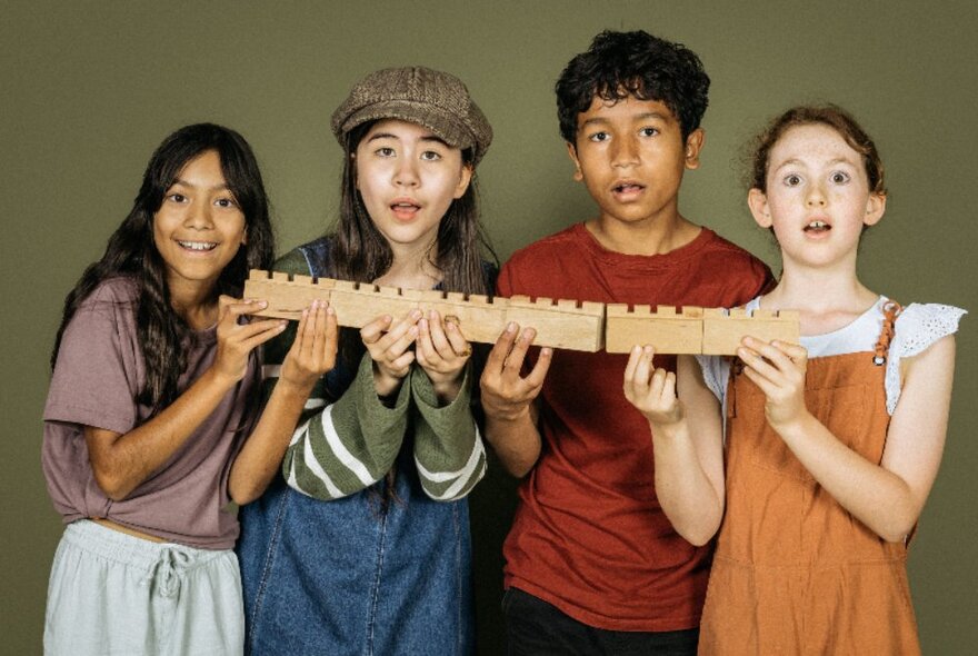 A group of four older kids all handing open mouthed and holding a long piece of carved wood. 