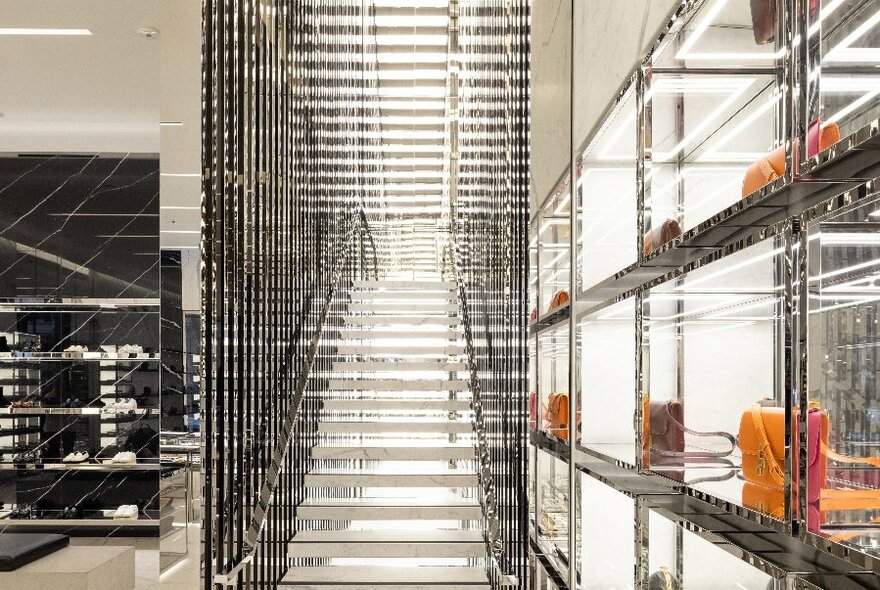 A shiny staircase in a store with a shelf holding orange handbags 