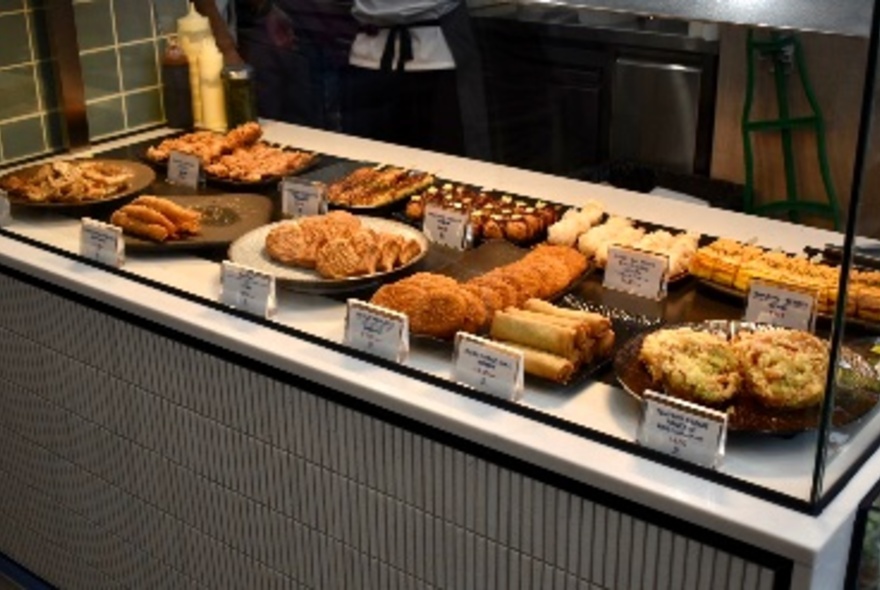 The food display counter at Maki Roll with trays of food behind glass.
