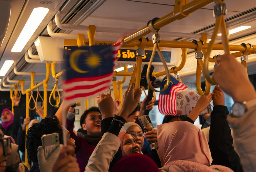People on a tram waving Malaysian mini flags.