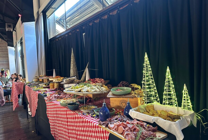 A Christmas themed buffet table with a red and white checked tablecloth and three small illuminated Christmas trees. 