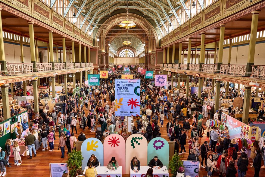 A busy market with colourful signs in a building with a domed ceiling.