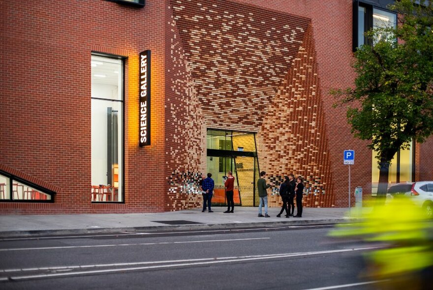 A tall brick building with people outside and a large detailed entrance. 