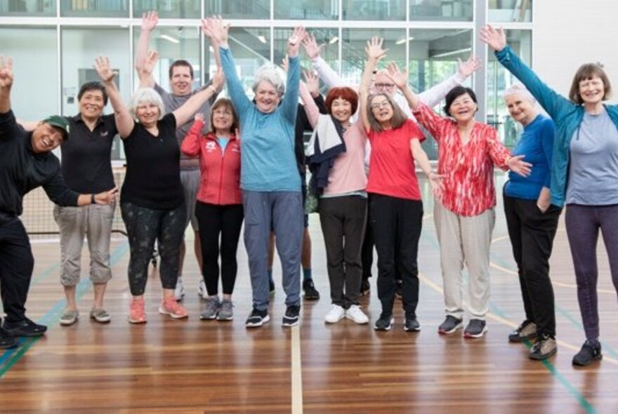 A group of seniors lined up waving arms in an indoor exercise hall.